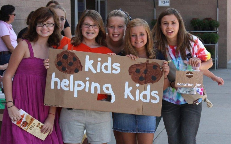 Kids holding a sign that says kids helping kids