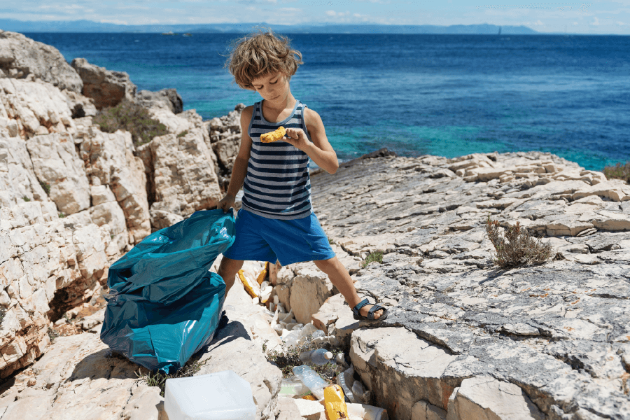 boy picking up trash near the ocean