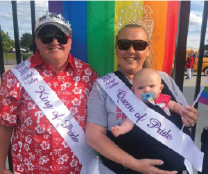 Lesbian couple holding a baby in front of LGBT flag