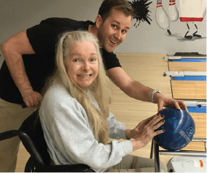 woman in wheelchair bowling with someone's help