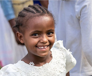 Smiling little girl in a white dress International Crisis Aid Inc