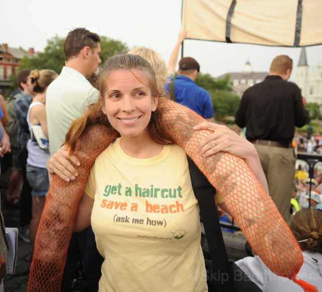 A woman poses wearing a T-shirt saying "get a haircut, save a beach."